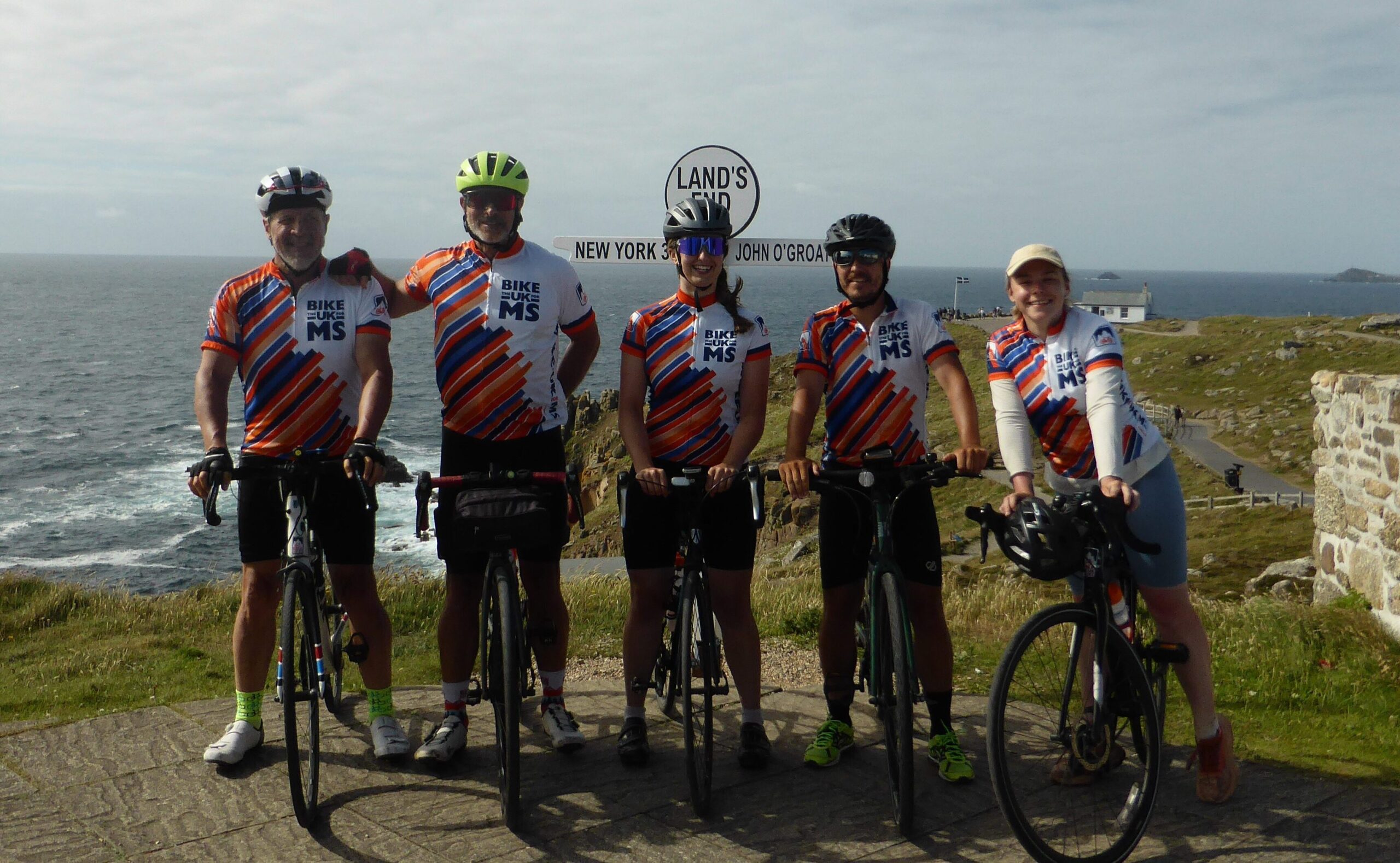 Bike the UK for MS cyclists posing next to the iconic Land's End sign post