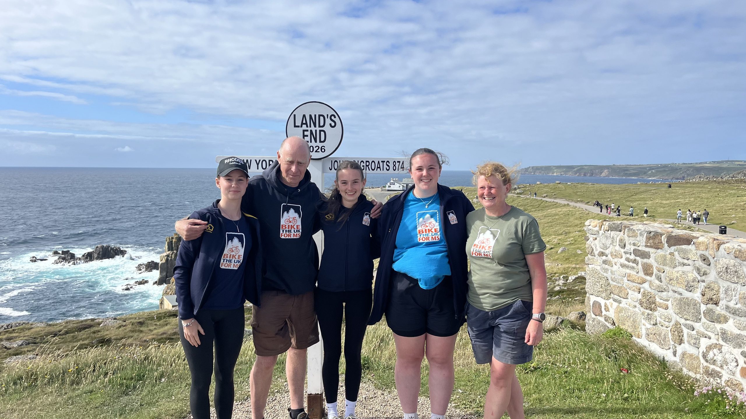 Bike the UK for MS Route Leaders standing together in front of the Land's End sign post at the end of the John O'Groats to Land's End cycle