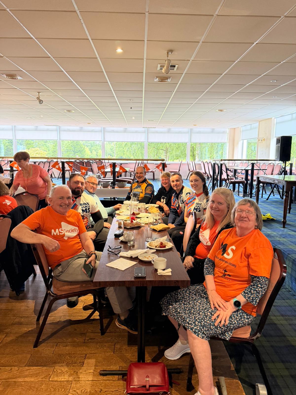 Bike the UK cyclists in their jerseys sitting round a table eating with members of the MS society with their MS t-shirts on